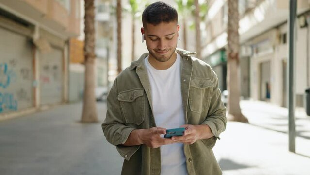 Young hispanic man smiling confident using smartphone walking at street