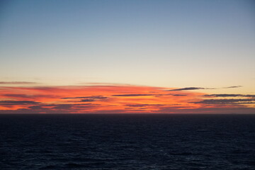 Naklejka premium Sunset in Atlantic Ocean during calm weather in Summer season with the sun behind the horizon. Sunrays have orange colour. Picture was taken from the navigational bridge of the cargo container vessel.