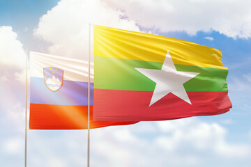 Sunny blue sky and flags of myanmar and slovenia