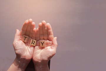 female hands hold wooden tiles with word Try on grey background