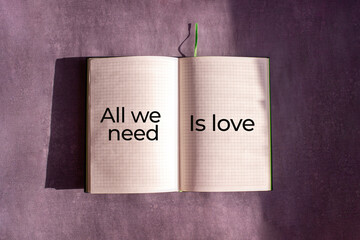 An open notebook is on the gray background. The word "All we nedd is love" is written on a blank sheet of notebook. Learning, education concept.