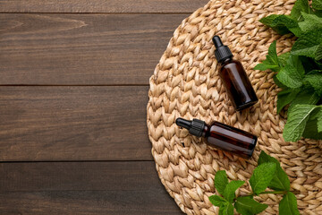 Bottles of essential oil and mint on wooden table, top view. Space for text