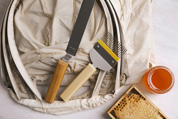 Different beekeeping tools and jar of honey on white table, flat lay
