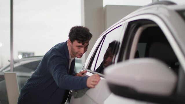auto center, young joyful male customer looks at a new car with enjoyment in vehicle dealership