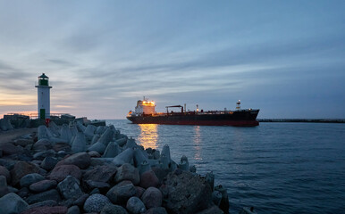 Large oil chemical tanker ship arriving to the cargo port terminal at sunset. Breakwaters,...