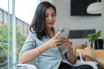 Beautiful young businesswoman using smart phone, reading news, checking social media while sitting in modern office.