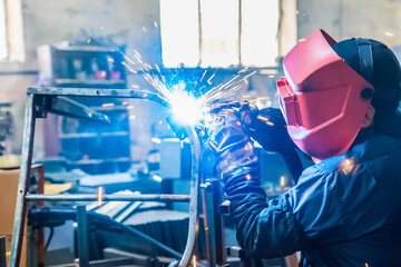 A welder in production is engaged in the manufacture of products. In a mask, in gloves, sparks fly