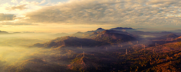 Aerial view panorama Morning scenic on high mountains with electricity pylon Pang Puay, Mae Moh, Lampang, Thailand. Beautiful morning with golden sunrise and fog flowing. - obrazy, fototapety, plakaty