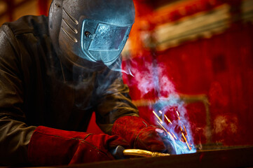 Employee in protective mask and gloves welds metal carcass - obrazy, fototapety, plakaty