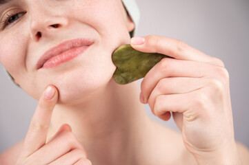 Close-up portrait of a young woman massaging her face with a gouache scraper. 