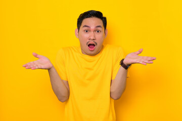 Shocked young Asian man in casual t-shirt with open mouth and raised palms isolated on yellow background. People lifestyle concept