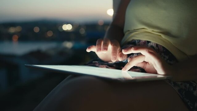 Close-up of a girl working on a tablet at sunset by the sea. Leisure and business female hands click on the computer. High quality 4k footage