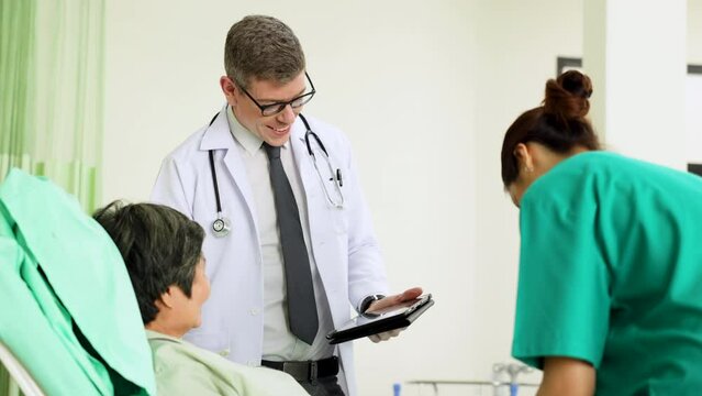 Senior Male doctor professors holding clipboard giving advice to treat patients with general woman doctor in modern hospital ward. Healthcare medical and medicine