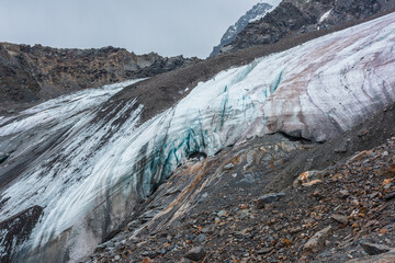 Awesome dramatic landscape with beautiful hanging glacier. Hole in dirty glacier near sharp mountain range. White blue glacial ice on smooth rocks of orange color. Cavity in ice cornice in center.