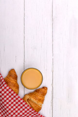 Fototapeta na wymiar Glass of orange juice and croissants under red gingham napkin on white wooden breakfast table. Flat lay with copy space 