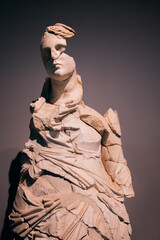 A majestic stone statue of a beautiful woman or goddess with a half-split and damaged face. The...