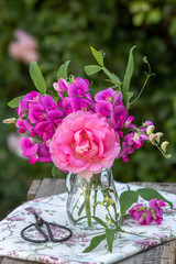 Blumenstrauß mit pink Rose und Wicken in Glasvase im Garten