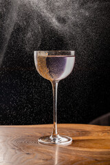 Gently lilac drink in a beautiful thin glass, decorated with nut crumbs with splashes on the background. Bar or restaurant concept