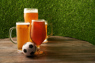 Four glasses of beer with soccer ball on the green grass background.