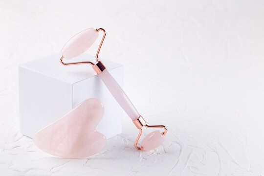Rose quartz crystal facial roller and massage tool Gua sha with podium on white background,