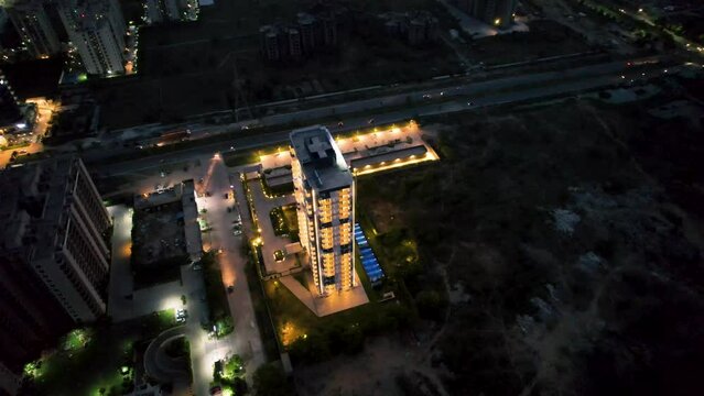 orbiting aerial dusk shot of brightly lit skyscraper in dark environment showing new construction and development of real estate in outskirts of the city