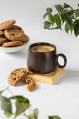 A cup of coffee, chocolate chip cookies in a round dish in the background.