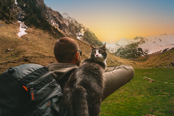 Man walking outdoors in mountains with his cat friend on the shoulder. Scene in nature at sunset....