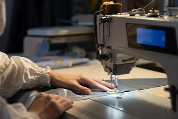 Woman tailor work on sewing machine stitching patterns of new collection. Closeup shot of female sewer hand dressmaking. Seamstress use professional equipment for tailoring. Garment industry concept