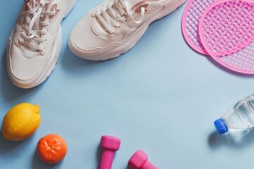 Flat lay fitness mockup photography for design. White sneakers, fruits, water bottle, dumbbells and tennis rackets on a blue background. Free space for text