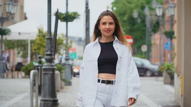 Smiling simon young woman in formal outfit walking outside on street and feeling happy. Modern urban town landscape, female wearing spring clothes