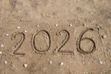 The numbers 2026 are written by hand on the sand, on the seashore, around the shell. The concept of vacation, holidays, new year, tourism, advertising, travel. High quality photo