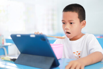 Asian kid with dirty sauce or food stain on shirt from eating in meal while watching tablet. dirty stain for cleaning concept. - obrazy, fototapety, plakaty