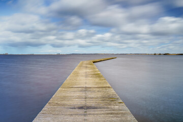 Fototapeta na wymiar Wooden jetty at the lake with exaggerating cumulus clouds