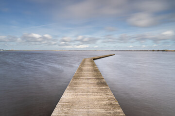 Obraz premium Long Wooden construction jetty at the lake with Dutch cloudy skies