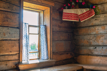 A window with light curtains with a pattern of blue flowers. View from the window of the village in the countryside. The window of a wooden log old house.