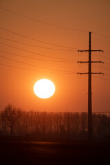 Harnassing the power of sun. Telephoto of a setting sun, contrasted with an image of a powerline, to symbolize solar power.