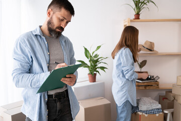 Happy man checking stuff in cardboard box before sent to transportation company and moving to new...