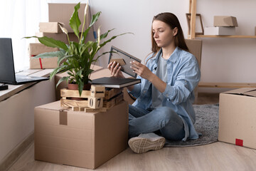 Fototapeta na wymiar Young woman moving to new place sitting on floor hugging holding frame looking at photo cheerful