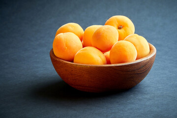 Bright ripe apricots in a wooden bowl on a dark background
