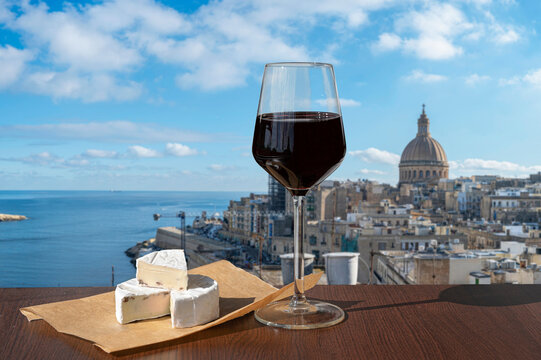 Glass of red wine with cheese with view of Valletta old town and harbor in Valletta, Malta.