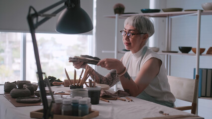 Asian elderly woman enjoying pottery work at home. A female ceramicist is making new pottery in a studio.
