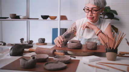 Asian elderly woman enjoying pottery work at home. A female ceramicist is making new pottery in a studio.