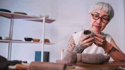 Asian elderly woman enjoying pottery work at home. A female ceramicist is making new pottery in a studio.