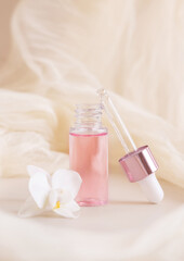 Obraz na płótnie Canvas Pink Dropper Bottle near white orchid flower on light yellow close up. Skincare beauty product