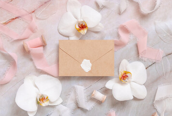 Blank sealed envelope near white orchid flowers and silk ribbons on marble, mockup
