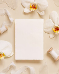 Wedding card near white orchid flowers and silk ribbons on light yellow, mockup