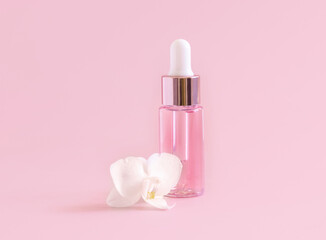 Pink Dropper Bottle near white orchid flower on light pink close up. Skincare beauty product