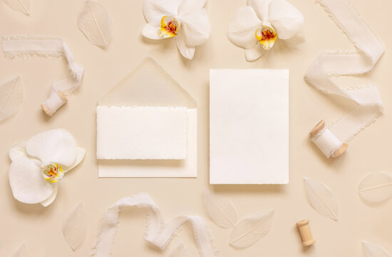 Wedding cards near white orchid flowers and silk ribbons on light yellow, suite mockup