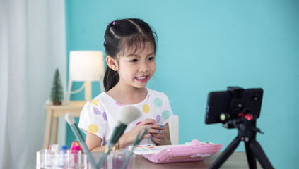 Happy little Asian girl beauty blogger recording video for teaching to use cosmetic make up.