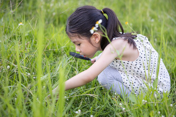 Cute little Asian girl using magnifier glass to look for something inside flower fields.